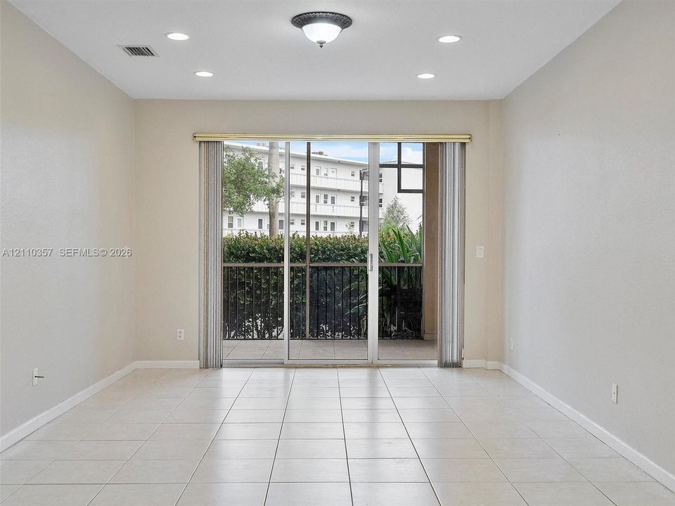 Neutral-toned tile flooring, recessed ceiling lighting, and floor-to-ceiling glass sliding doors opening to a private balcony
