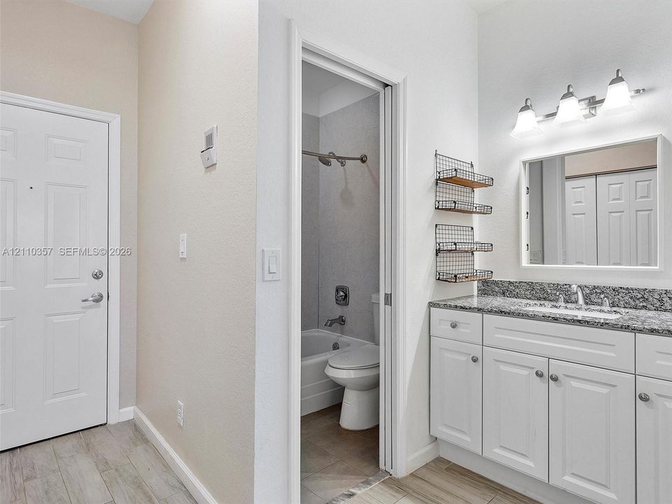 Bathroom featuring white cabinetry, stone-finish countertop with an integrated basin, three-light vanity fixture, and wood-finish flooring