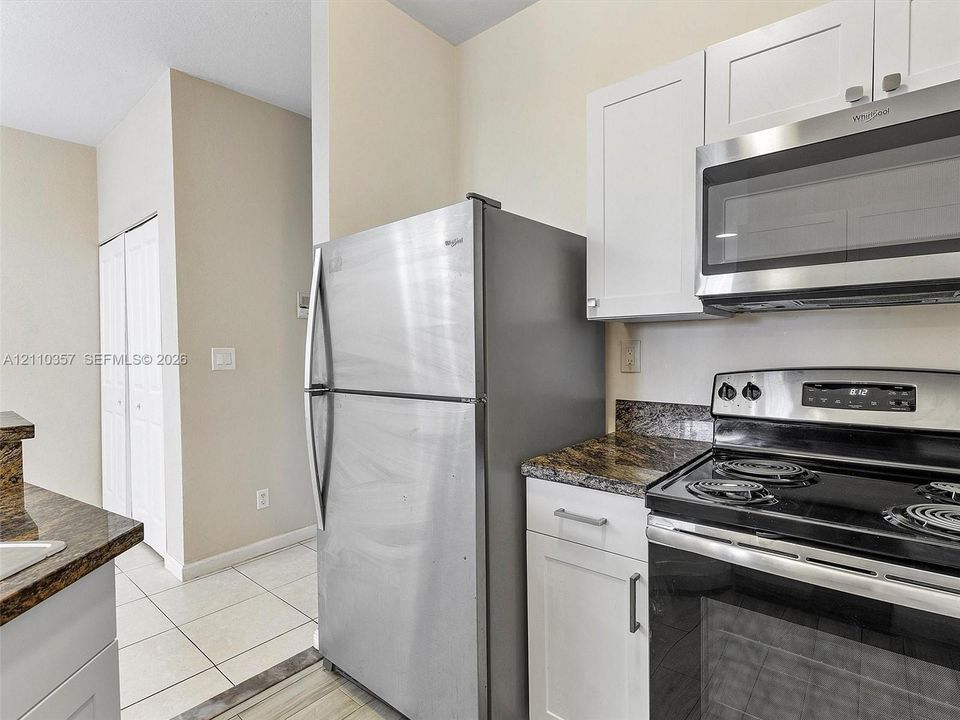 Kitchen featuring white shaker-style cabinetry, stone-finish countertops, stainless steel refrigerator, built-in microwave, and tile flooring