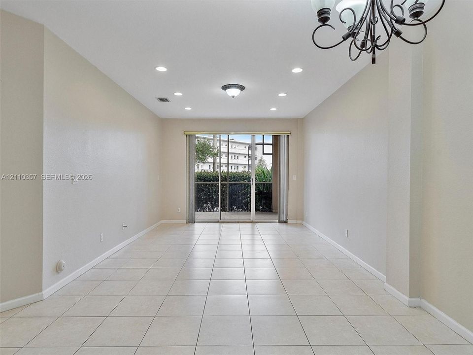 Neutral-toned room featuring tile flooring, recessed lighting, a decorative chandelier, and sliding glass doors with screen enclosure