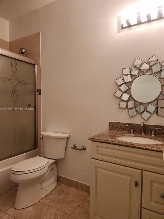 Bathroom featuring stone-surface vanity with undermount sink, shower with etched glass sliding doors, tiled flooring, and wall-mounted light fixture