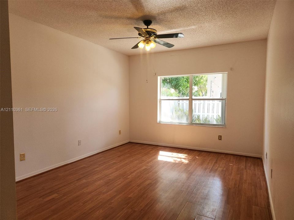 Room featuring wood-finish flooring, a ceiling fan with integrated lighting, and a window with exterior paneled fencing