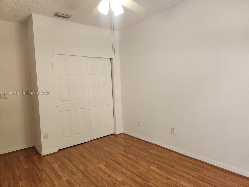 Room featuring wood-finish flooring, white walls, and a closet with dual-panel sliding doors, complemented by an overhead ceiling fan