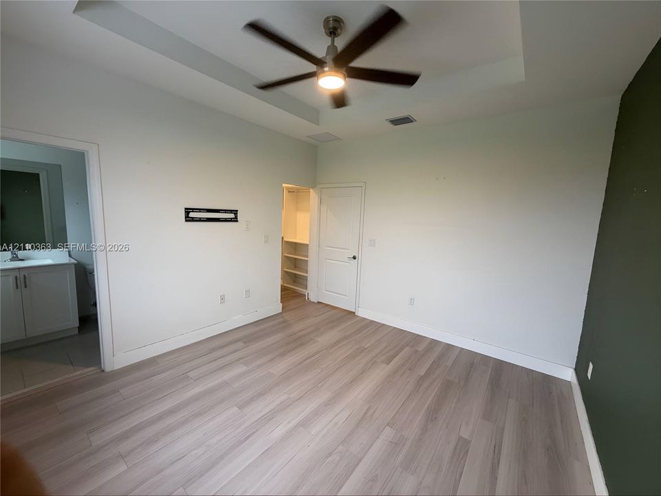 Tray ceiling with integrated fan, wood-finish flooring, and built-in closet shelving