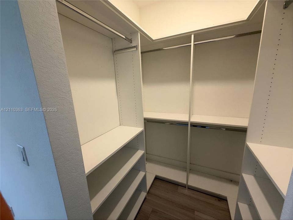 Walk-in closet featuring white built-in shelving, adjustable shelving units, integrated metal clothing rods, and wood-finish flooring