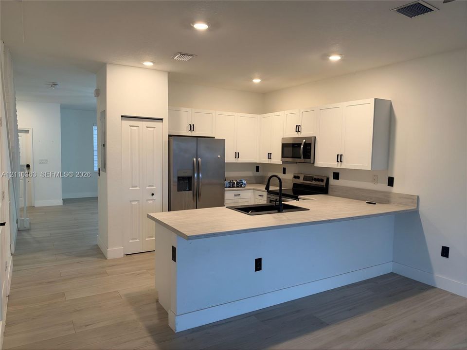Kitchen featuring white shaker-style cabinetry, stainless steel appliances, wood-finish flooring, a neutral-toned countertop, and a matte black faucet