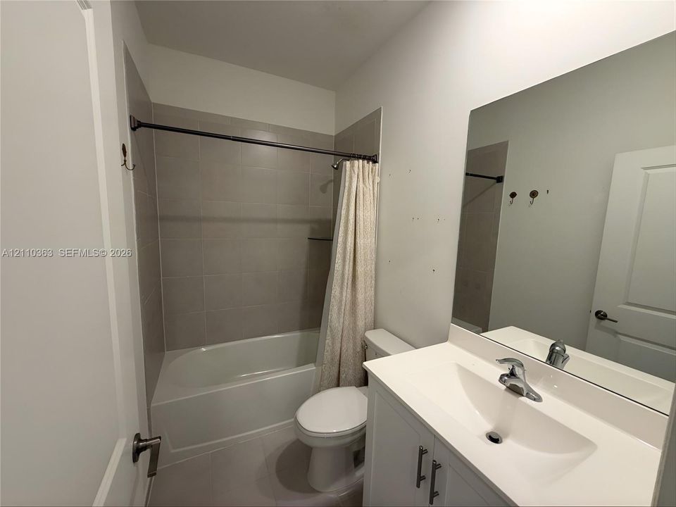 Bathroom featuring a white vanity cabinet with a integrated sink, polished chrome faucet, large vanity mirror, and a tub-shower combination with light gray tile surround