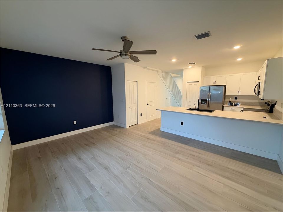 Open-concept space featuring wood-finish flooring, a dark-toned accent wall, a breakfast bar with light-colored countertops, shaker-style cabinetry, and recessed lighting