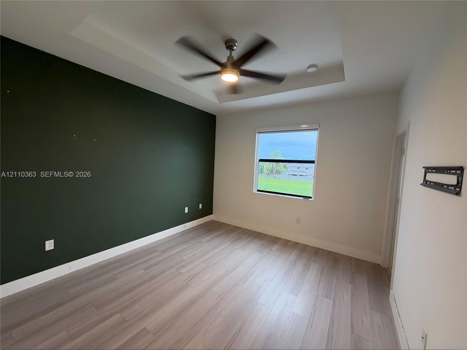 Tray ceiling with a central multi-blade ceiling fan, wood-finish flooring, and a solid-color accent wall
