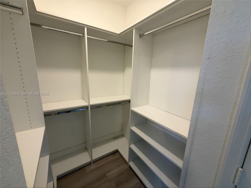 Walk-in closet featuring white built-in shelving, adjustable storage cubbies, integrated metal hanging rods, and wood-finish flooring
