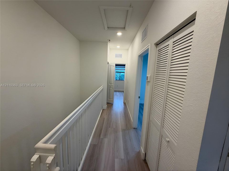 Hallway featuring wood-finish flooring, white louvered-door closet, recessed lighting, and painted white railings