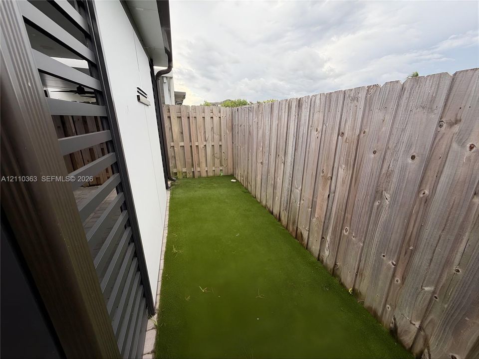 Enclosed exterior space featuring vertical wood-slat fencing, synthetic turf, and a gated metal side screen
