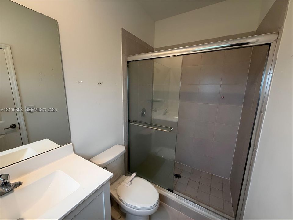 Bathroom featuring a vanity with a white countertop and integrated sink, a full-height wall mirror, a walk-in shower with tiled surround and sliding glass doors, and a porcelain toilet