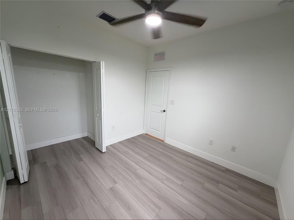Interior room featuring wood-finish flooring, a multi-panel door, a closet with double doors, and a ceiling fan with integrated lighting