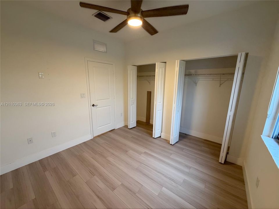 Interior space featuring wood-finish flooring, dual closets with bi-fold doors, and a ceiling-mounted light fixture with a fan