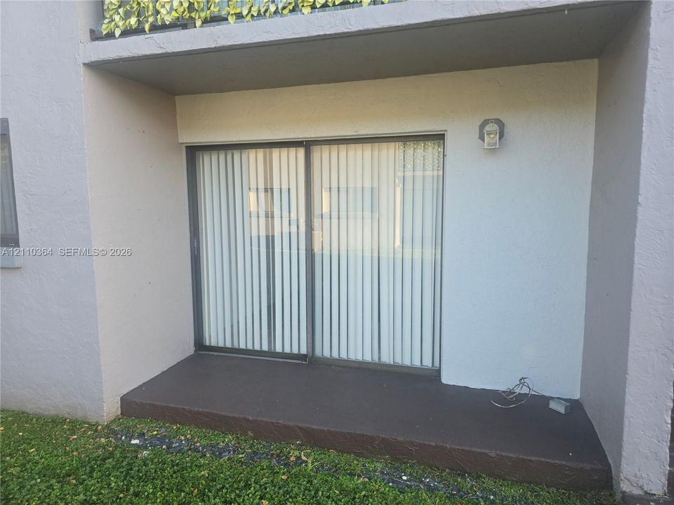 Covered concrete patio featuring sliding glass doors and an exterior wall-mounted light fixture