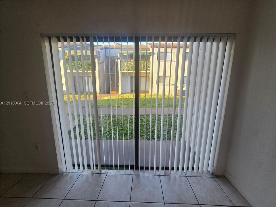 Large sliding glass door featuring vertical blinds and neutral-toned tile flooring
