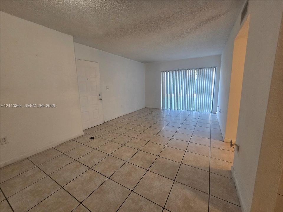 Neutral-toned tile flooring, white wall finishes, and vertical sliding glass door with integrated blinds