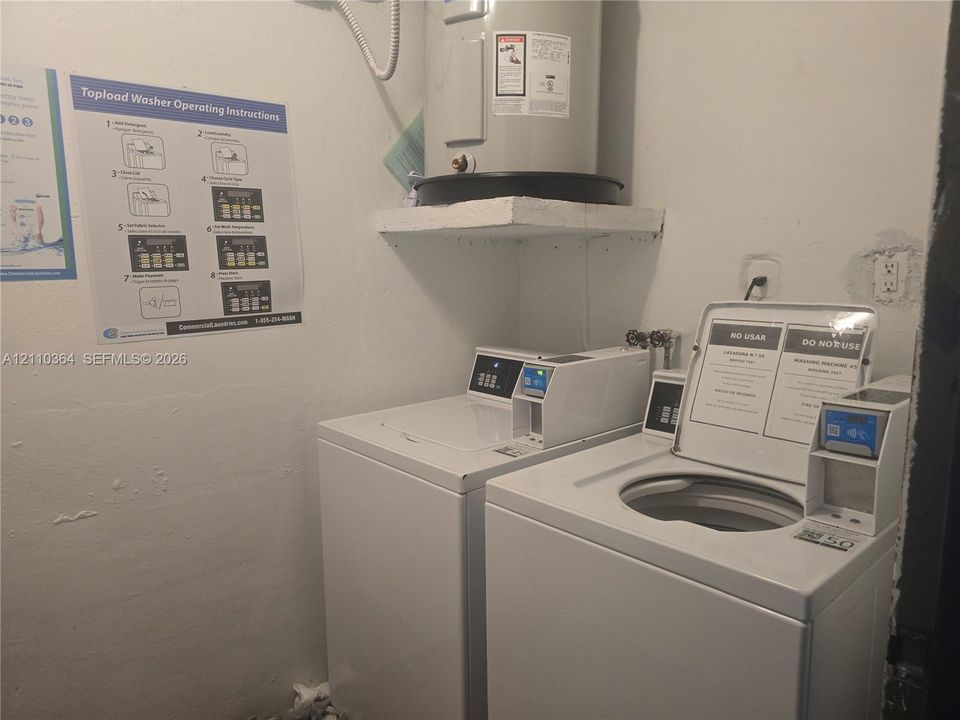 Utility area featuring an electric water heater on a wall-mounted platform and dual coin-operated laundry appliances