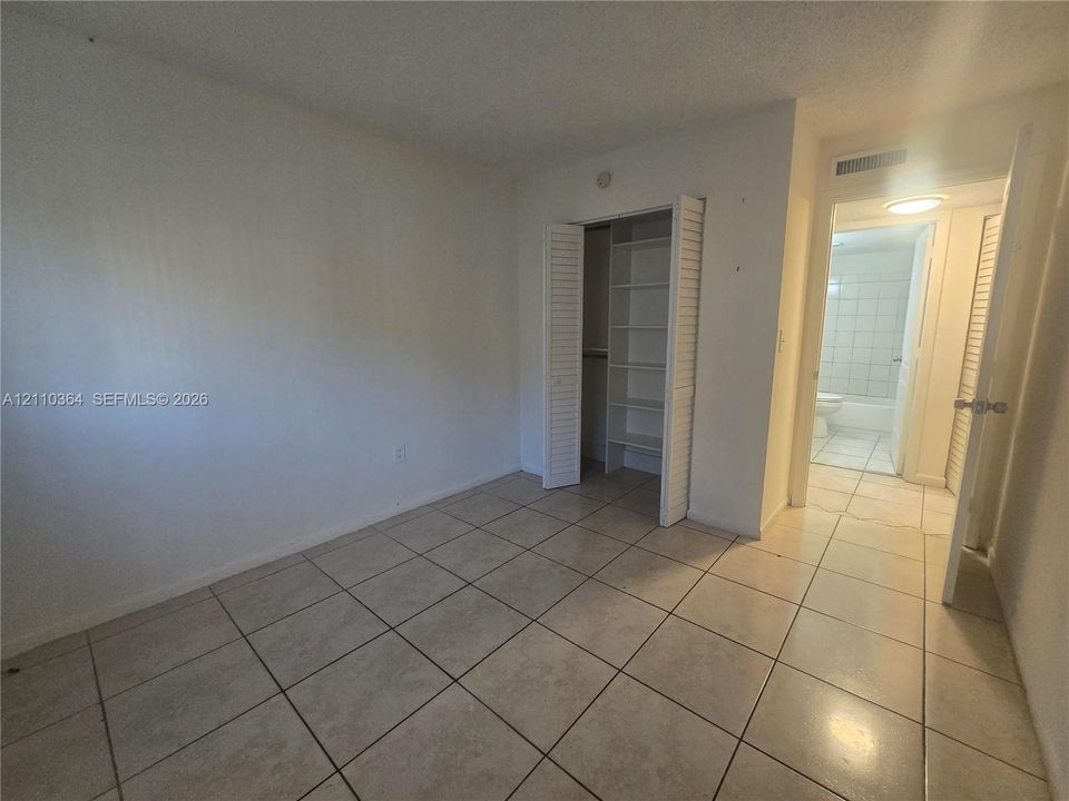Room featuring tile flooring and a built-in closet with louvered doors and interior shelving
