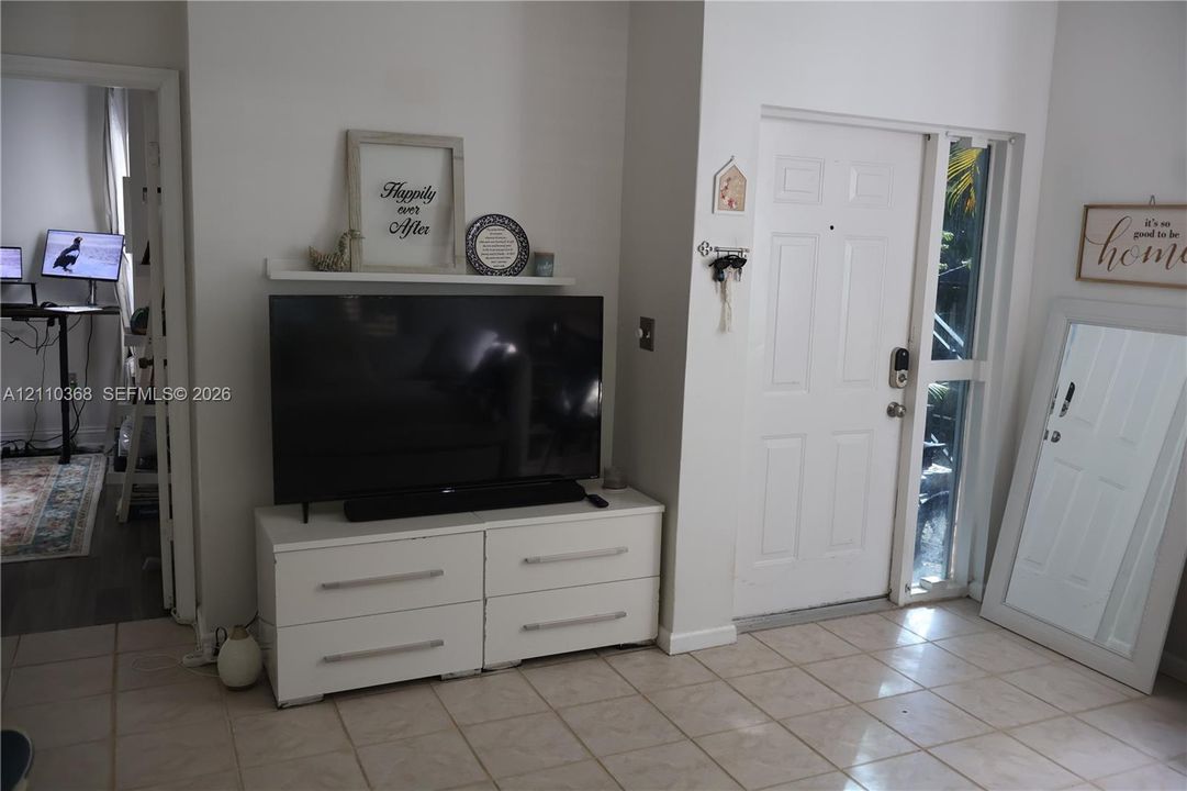 Entryway featuring light-toned tile flooring, a solid panel front door with an integrated sidelight, and a fixed wall-mounted display shelf