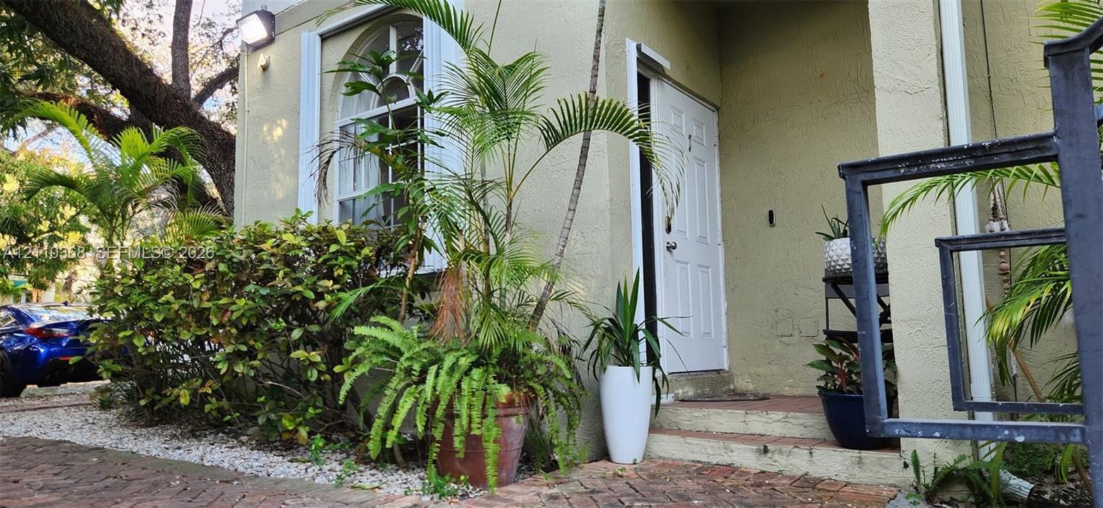 Exterior entryway featuring stucco siding, an arched window with decorative molding, and a brick-paved landing
