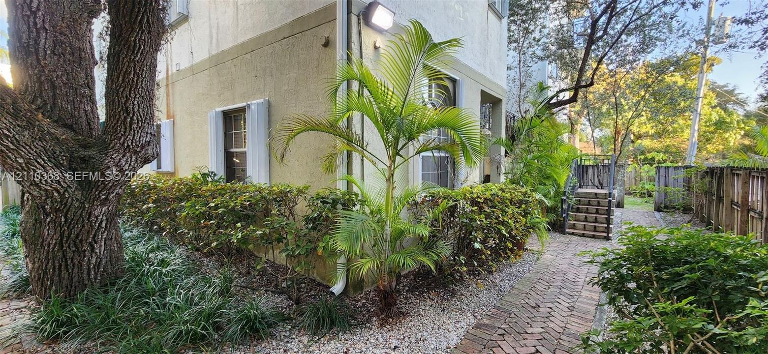 Stucco exterior featuring mature landscaping, a brick paver pathway, and an exterior staircase