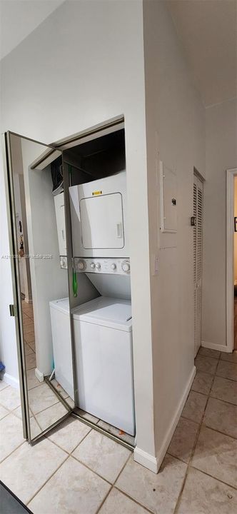 Laundry closet featuring a stacked washer and dryer, mirrored bifold door, and ceramic tile flooring