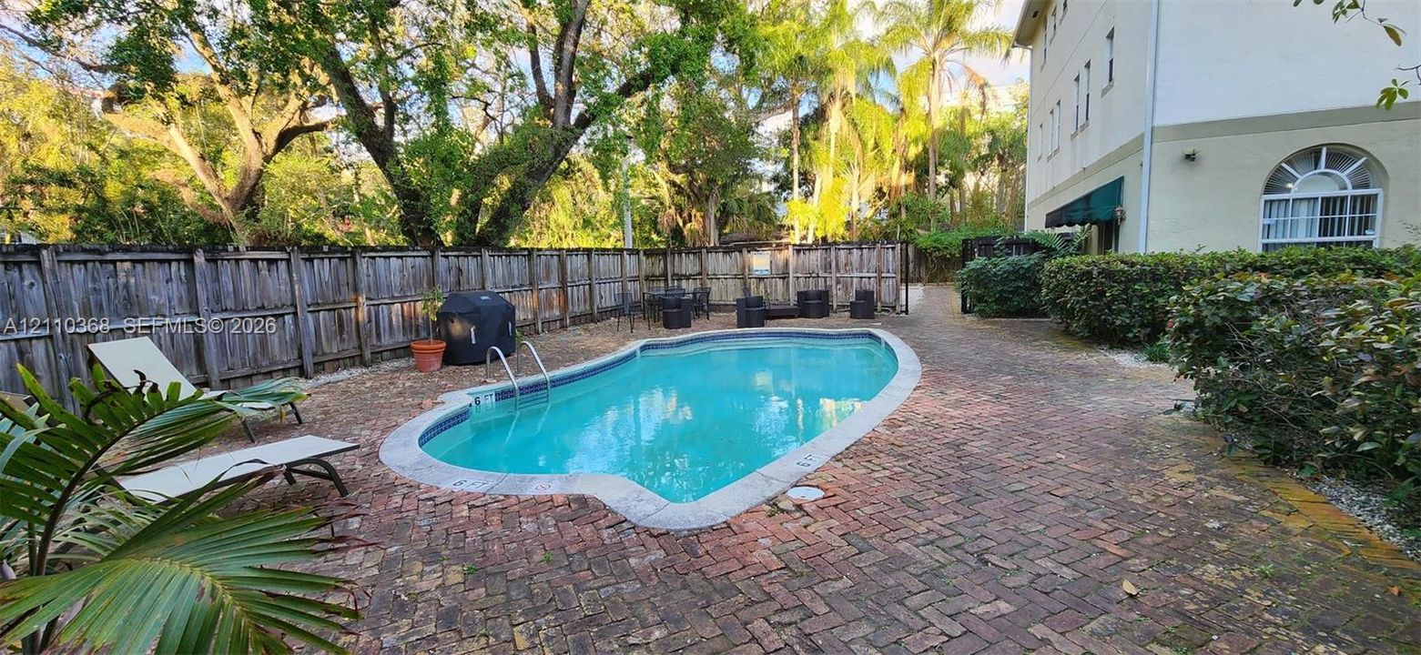 In-ground swimming pool featuring a brick paver deck, enclosed by a wood privacy fence and mature landscaping