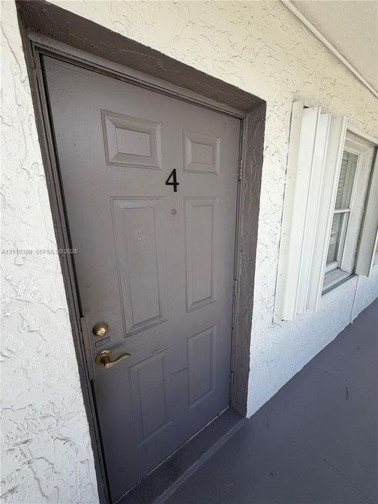 Stucco exterior finish with a paneled entry door, metallic lever handle hardware, and accordion-style storm shutters
