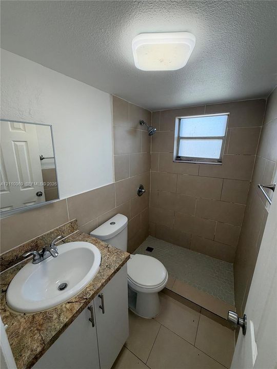 Vanity with stone-finish countertop, integrated oval sink, and chrome faucet, accompanied by a step-in shower with tile surround, a built-in toilet, and square ceiling-mounted light fixture