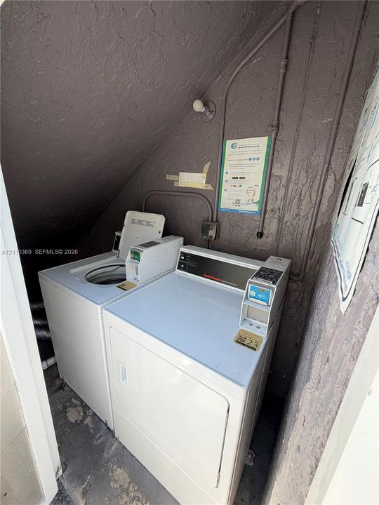 Dedicated laundry area featuring built-in coin-operated appliances, exposed conduit, and wall-mounted light fixture