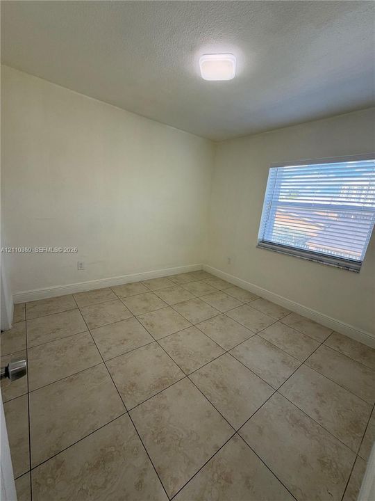 Neutral-toned ceramic tile flooring, single window with horizontal blinds, and a flush-mount ceiling light fixture