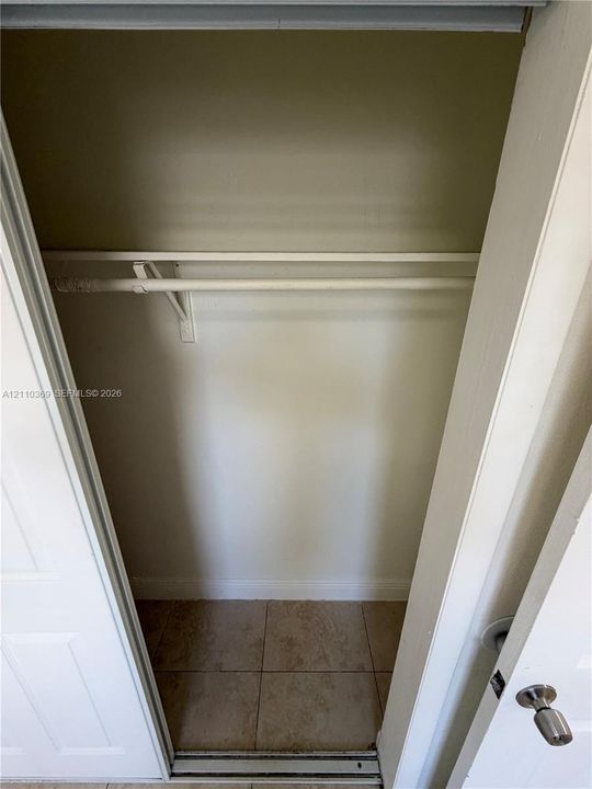 Reach-in closet featuring a neutral wall finish, tile flooring, and a white integrated hanging rod with shelf support