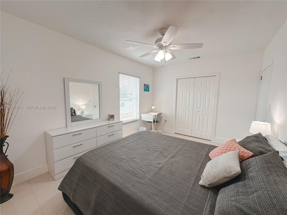 Neutral interior featuring white walls, window with horizontal blinds, ceiling fan with integrated lighting, and dual-panel closet doors