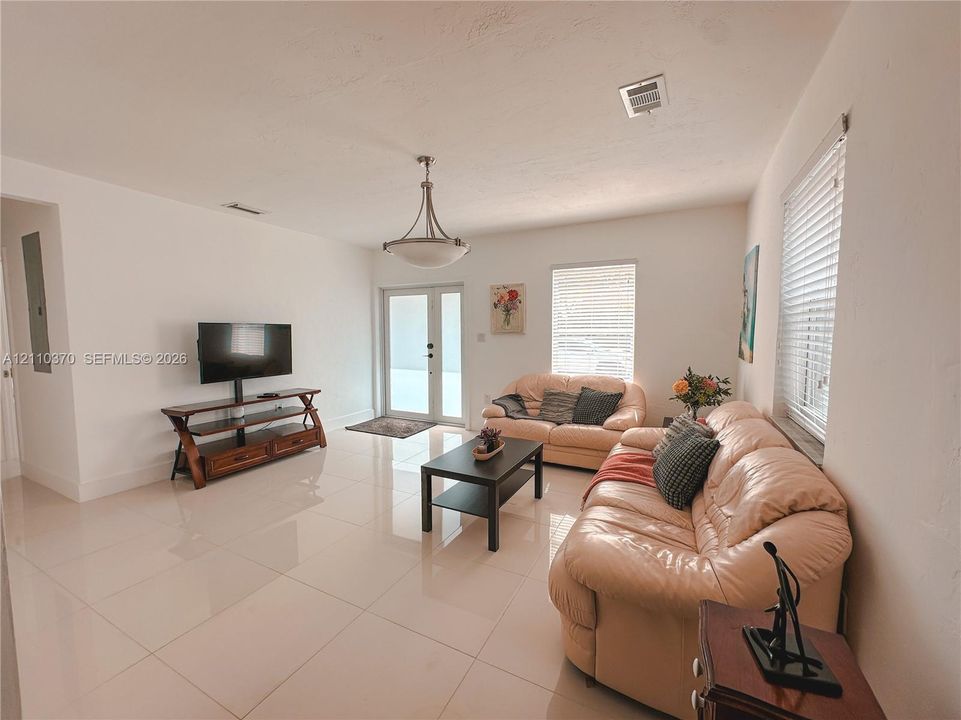 Neutral-toned tile flooring, semi-flush mount bowl lighting, and glass-paneled exterior doors with horizontal blinds