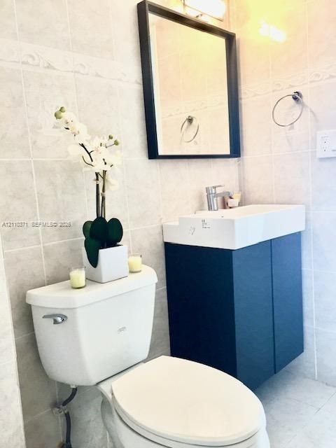 Wall-mounted navy blue vanity with a rectangular integrated sink, chrome faucet, framed mirror, and light-toned ceramic tile wall surround