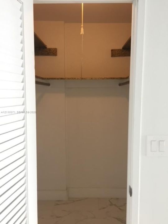 Storage closet featuring louvered bi-fold doors, built-in shelving, a hanging rod, and stone-finish tile flooring
