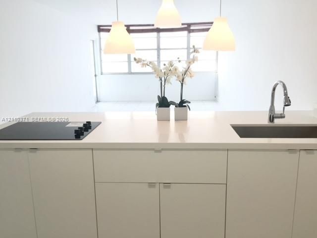 Kitchen island featuring a solid-surface countertop, integrated flat-surface cooktop, undermount stainless steel sink with a high-arch gooseneck faucet, minimalist flat-panel cabinetry, and three pendant lights