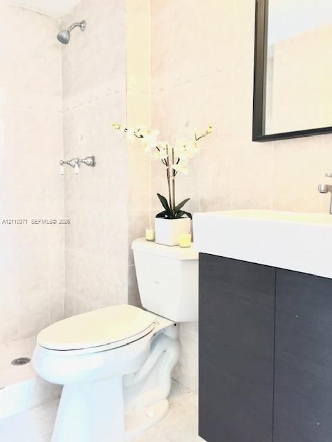 Full-height stone wall tiling, shower fixture with wall-mounted controls, dark wood-finish floating vanity, integrated rectangular sink, and rectangular vanity mirror with a dark frame