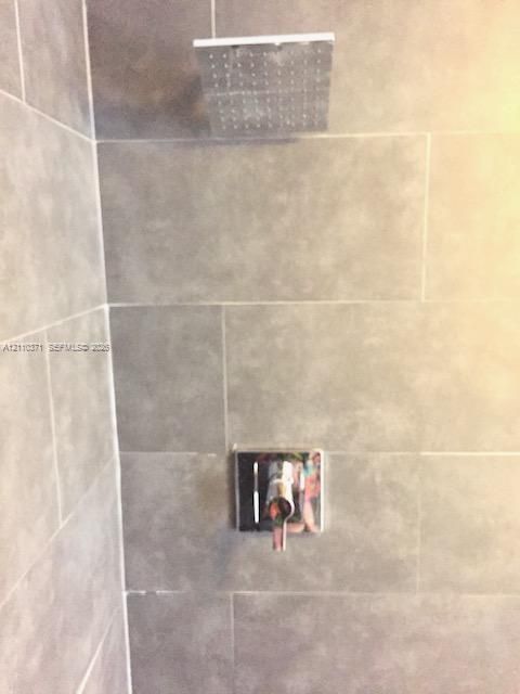 Large-format grey stone-finish wall tiling featuring a polished chrome rainfall shower head and a matching single-handle control valve