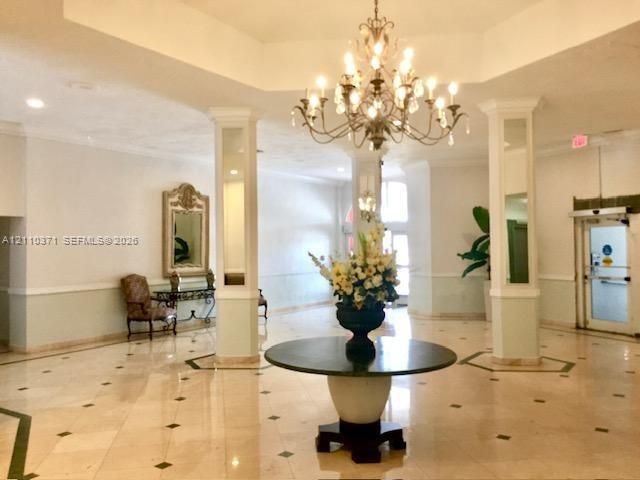 Grand lobby featuring a tiered tray ceiling, intricate crystal chandelier, polished stone flooring with decorative inlays, and mirrored support columns