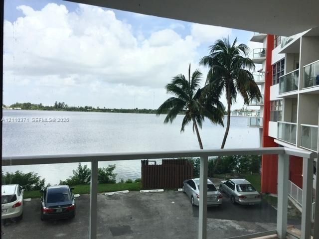 Covered balcony with a white metal railing and glass panels, overlooking a water feature and mature palm trees