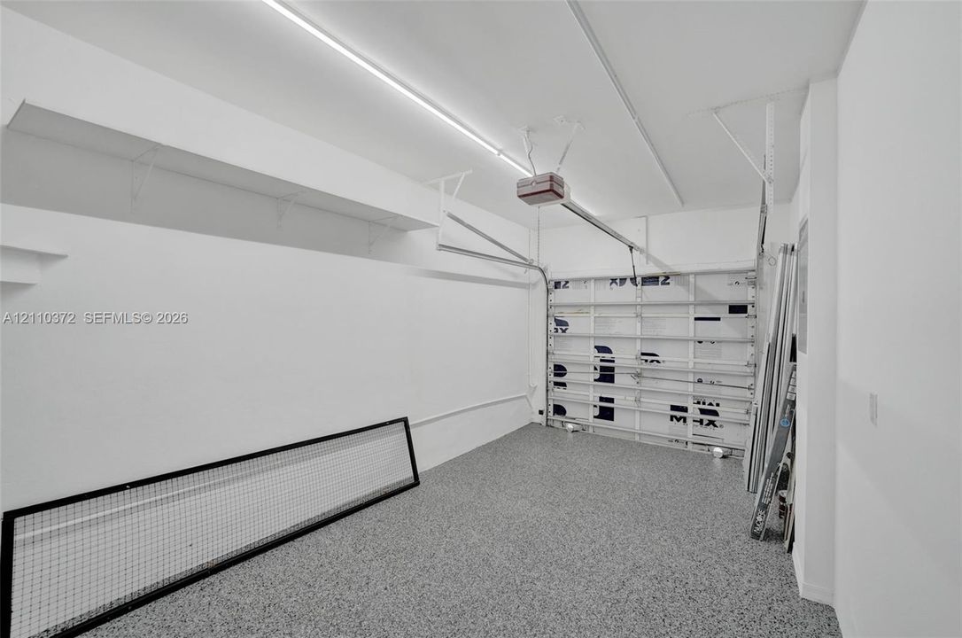 Enclosed garage featuring durable epoxy flooring, wall-mounted storage shelving, and an automated overhead door system