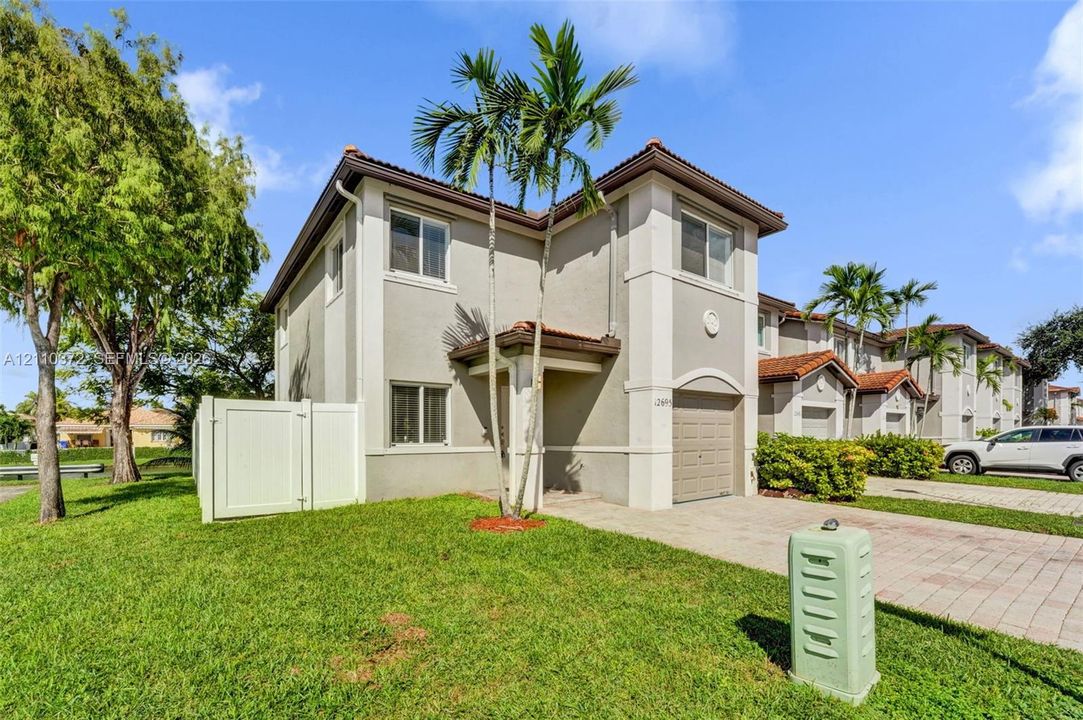 Two-story stucco exterior featuring a tile roof, an attached garage, and a paver driveway
