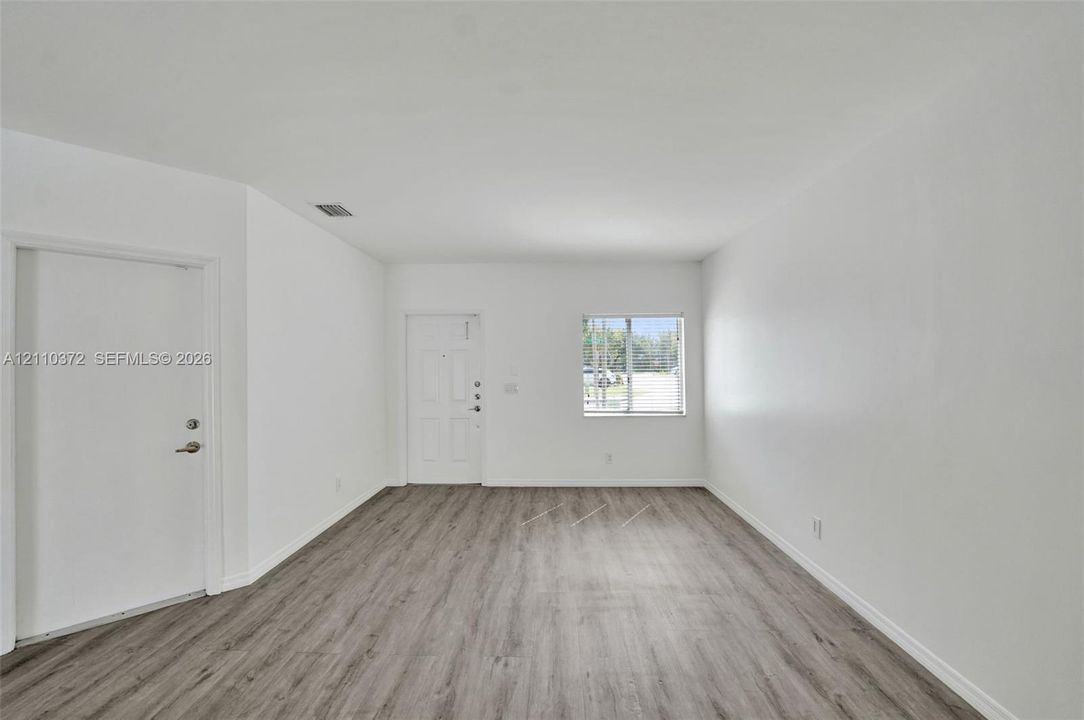 Neutral interior space featuring wood-finish flooring, a single window, and a multi-panel door