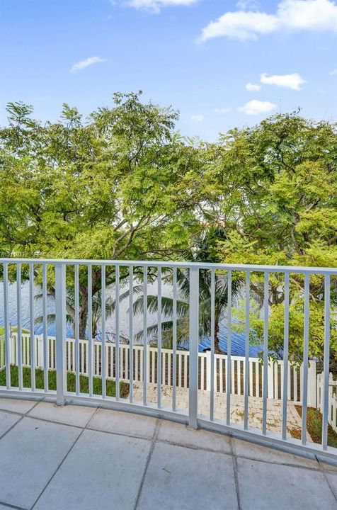 Balcony with large-format tile flooring and white metal railing, featuring water frontage and mature trees