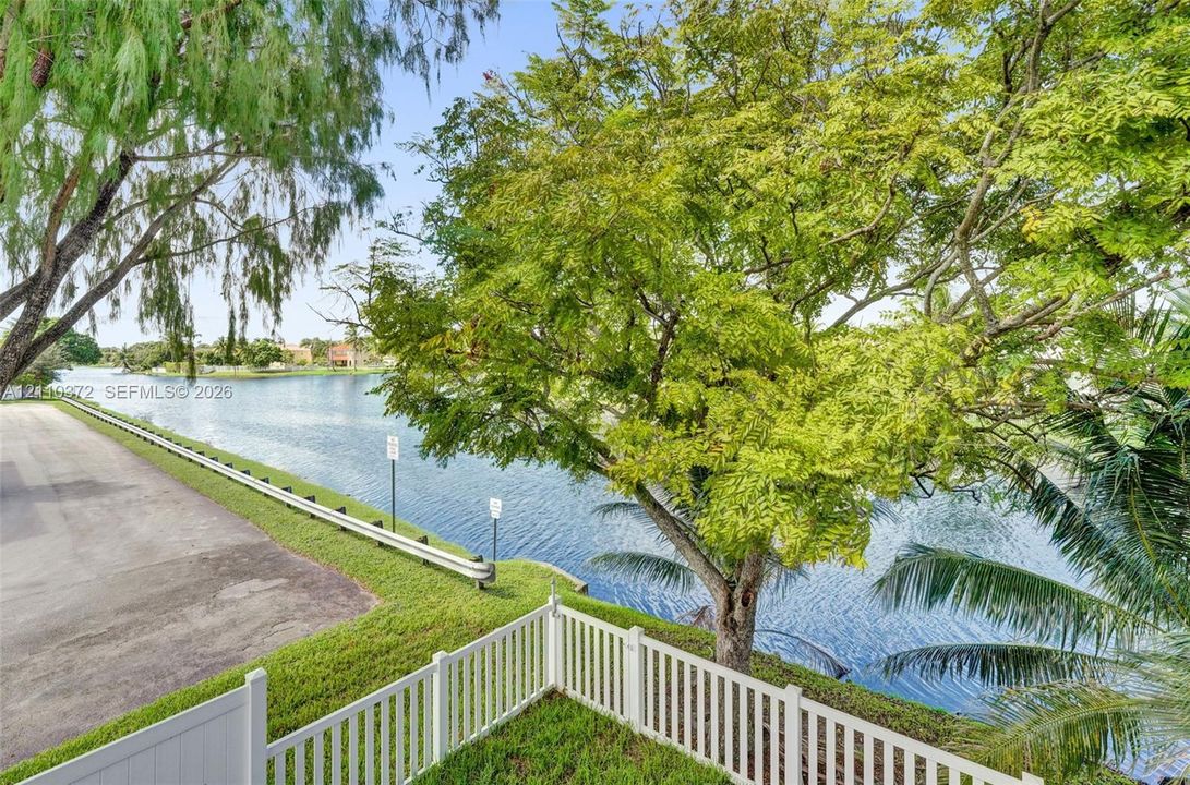 Waterfront lot featuring a white vinyl privacy fence, manicured lawn, and mature trees