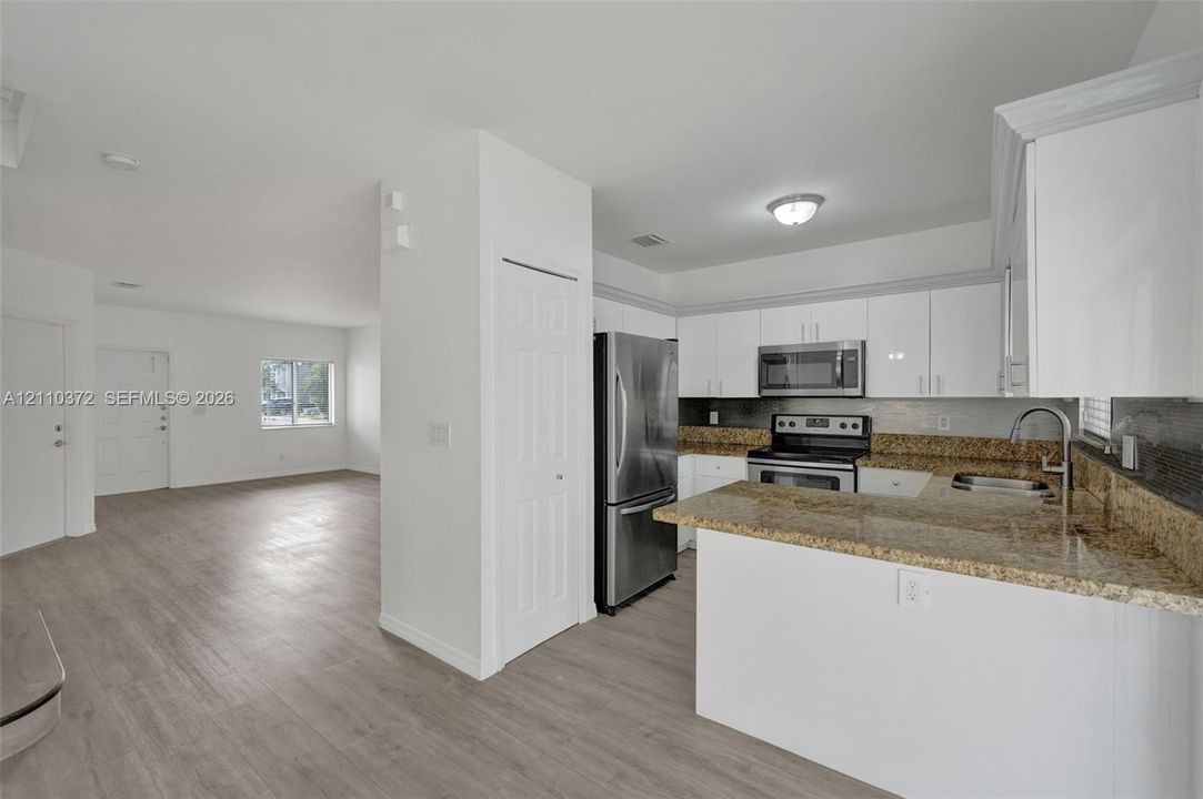 Kitchen featuring white cabinetry, stone-finish countertops, stainless steel appliances, and wood-finish flooring