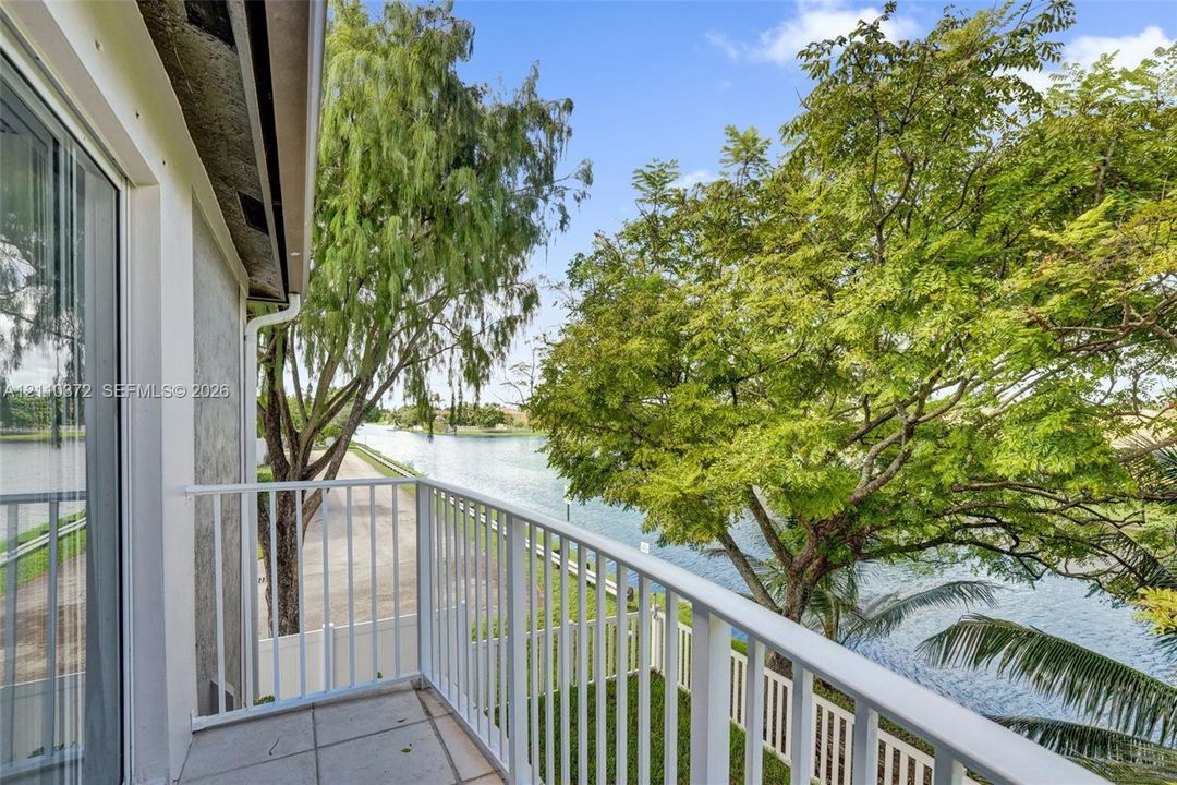 Exterior balcony featuring tile flooring and a white metal railing overlooking a canal and mature trees